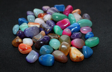 Colored rough gemstones in a heap of black surface detailed angle view with soft focus
