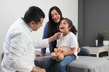 Latina mother cares for and accompanies her curly little daughter at the dark-haired pediatrician...