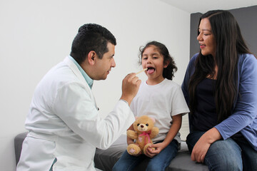 Latina mother cares for and accompanies her curly little daughter at the dark-haired pediatrician...
