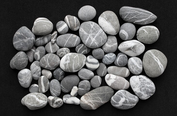 Bunch Of smooth gray granite stones with white quartz veins on black surface 
