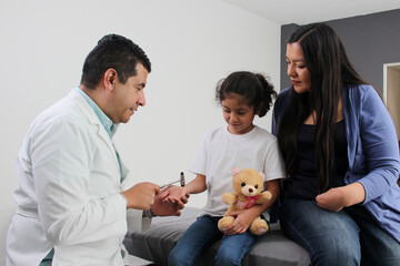 Latina mother cares for and accompanies her curly little daughter at the dark-haired pediatrician...