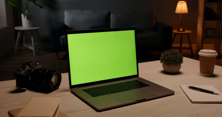 Close up shot of modern chroma key green screen laptop computer set up for work on desk at night - remote work, technology concept 