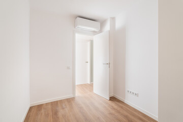 Empty bedroom with parquet flooring. An open door from the room leading to a corridor with other rooms. Air conditioning above the door saves from summer heat