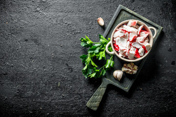 Crab meat in a bowl on a cutting Board with parsley and garlic cloves.