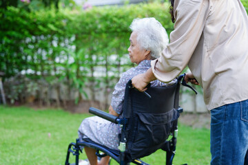 Fototapeta na wymiar Caregiver help Asian elderly woman disability patient sitting on wheelchair in park, medical concept.