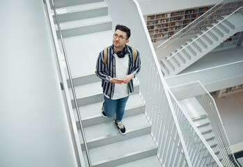 Library search, geek student or intelligent man for phd research, creative vision and knowledge in university. College, stairs above and person thinking of books for education, scholarship or study