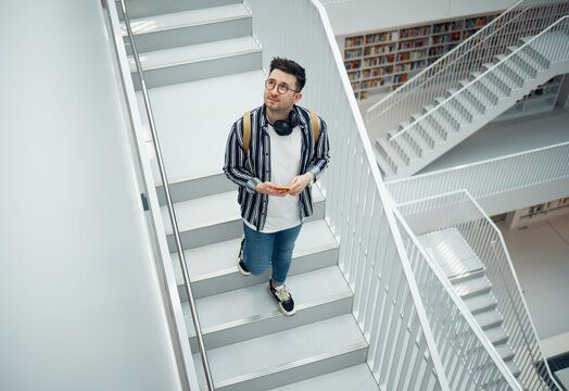 Library search, geek student or intelligent man for phd research, creative vision and knowledge in university. College, stairs above and person thinking of books for education, scholarship or study
