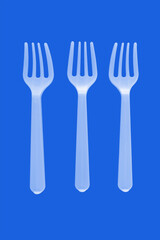 three plastic white forks on a blue background. isolate. Top view.