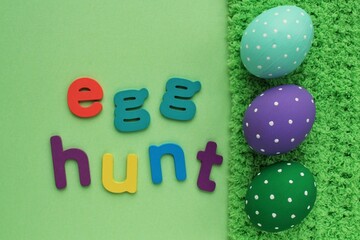 Egg hunt letters on green background and coloured eggs with polka dot on spring grass background. Easter greeting card, invitation, banner, poster sale. Flatlay, top view holiday concept. Sign for fun