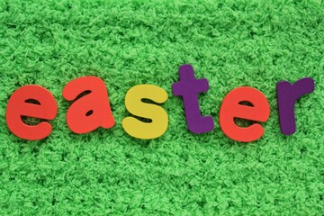 Easter colored lettering on green grass background. Holiday spring composition concept. Creative idea for greeting card, poster, banner, invitation, web. Top view, flat lay, close up