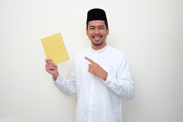 Moslem Asian man smiling while pointing to a book that he hold
