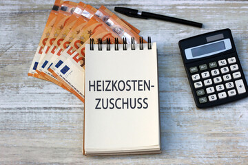 Das Wort Heizkosten Zuschuss ist auf einem Notizblock mit Taschenrechner und Euro-Banknoten abgebildet. - obrazy, fototapety, plakaty