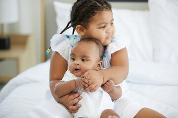 Fototapeta na wymiar African kid hugging a newborn baby or her sister on bed