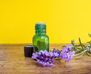 Lavender oil bottle and fresh lavender on yellow background	