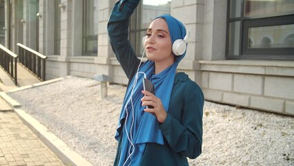 Middle eastern woman in hijab listening music with headphones and dancing. Woman independence and feminism concept. - Powered by Adobe