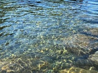Sea crystal clear healing water with smooth stones and pebbles at the bottom.