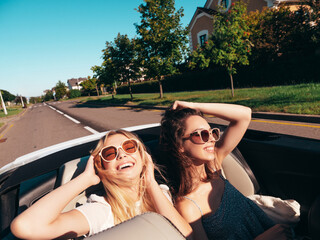 Portrait of two young beautiful and smiling hipster female in convertible car. Sexy carefree women...