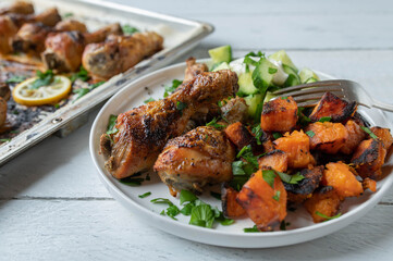 Chicken drumsticks with roasted sweet potatoes and cucumber salad on a plate