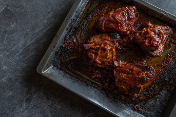 Thick pork ribs with homemade barbecue sauce on a baking tray isolated on dark background. Flat lay
