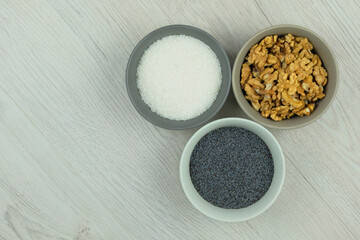 Coconut shavings,  poppy seeds and walnut in bowls on a woody background. Ingredients for adding to baking. Vegetarian product. Top view. Copy space.