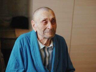 The 92-year-old grandfather is sitting in his room. Elderly care, personal hygiene and mental health. Close up portrait.
