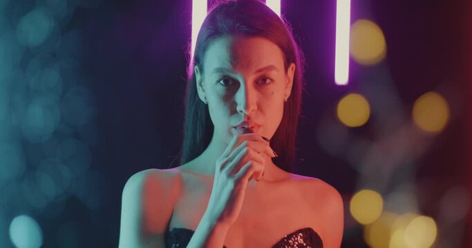 Portrait of fancy young lady smoking vape relaxing on glowing neon background. Electronic cigarette and modern youth lifestyle concept.