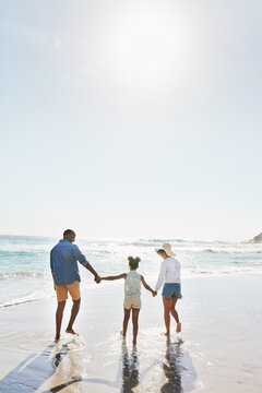 Beach Vacation And Couple With Child Walking In Water While Holding Hands Together With Love In Summer From The Back. Nature, Ocean And Blue Sky, Black Family On Tropical Island Holiday In Maldives.