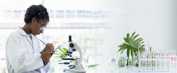 African American girl scientists learning and writing science and researching through microscope in...