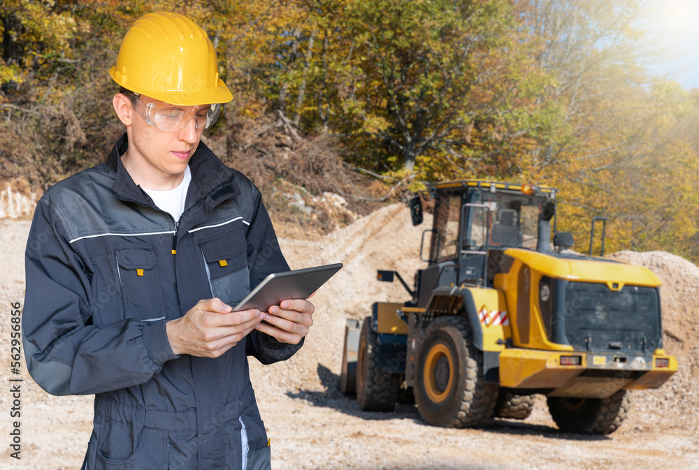 Wall mural Engineer in a helmet with a digital tablet on the background of construction machine	