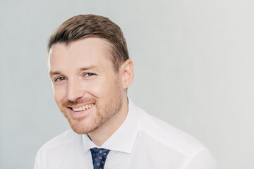 Positive young unshaven male entrepreneur has pleasant smile, dressed in elegant clothes, rejoices successful meeting with colleagues, discuss their business plans, isolated over white background