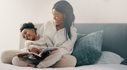 Preschool age girl laughs happily while sitting with her mom reading a story book - obrazy, fototapety, plakaty