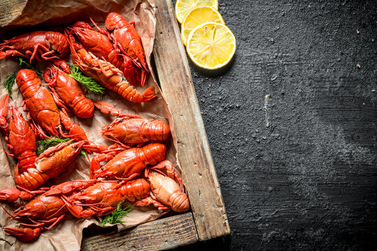 Boiled crayfish on a wooden tray with slices of lemon.