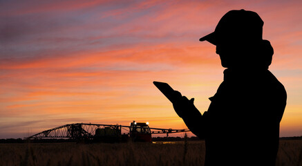 Farmer controls sprayer with a tablet at night. Smart farming and precision agriculture - obrazy, fototapety, plakaty