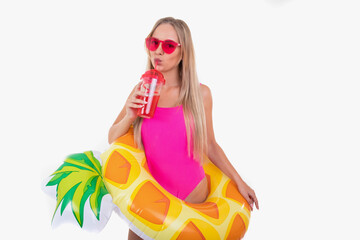 A  young woman in a pink swimsuit and glasses holds an inflatable swimming circle and drinks lemonade