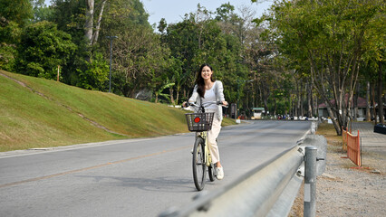 Fototapeta premium Happy and chill young Asian woman riding a bicycle on the road in public park