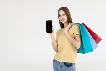 Naklejka premium Happy woman standing with satisfied look showing shopping bags and smart phone with blank screen for advertisement isolated on white background.