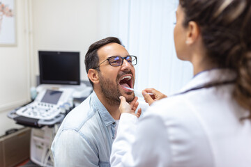 A young man sits on an exam table across from his doctor. The doctor reaches forward with a tongue...