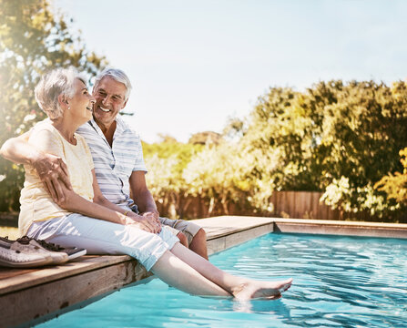 Senior couple, hug and smile by swimming pool for relax, love or quality bonding time together on summer vacation. Happy elderly man holding woman relaxing with feet in water by the poolside outside