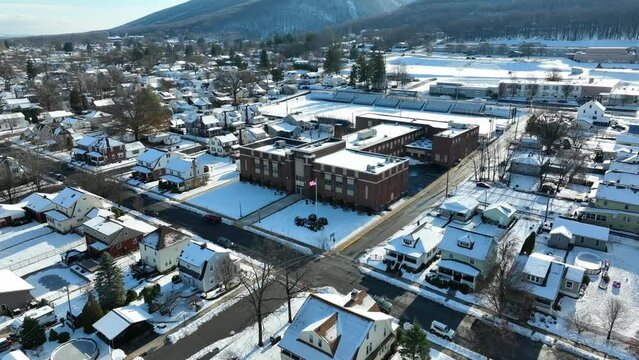 Aerial view of town in snow. American flag waves in front of brick school building on snow day.