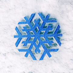 Artificial blue snowflake on a snowy background. For holiday decor