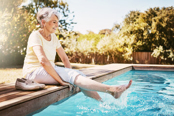 Relax, travel and senior woman by the pool while on a vacation, adventure or outdoor trip in summer. Happy, smile and elderly lady in retirement with her feet in the swimming pool at a holiday resort - Powered by Adobe