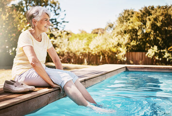 Happy elderly woman with her feet in the pool while on a vacation, adventure or outdoor trip in...