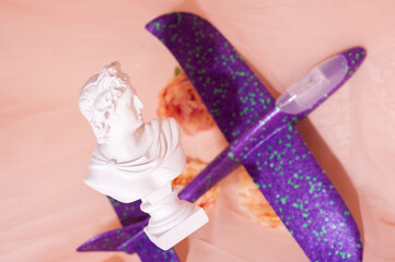 A figurine of Apollo hovering over a background with flowers with a purple toy plane. Copy space