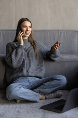 Happy woman talking on mobile phone while sitting at a couch at home with laptop