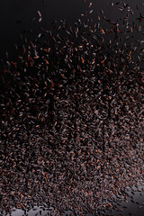 Riceberry rice pouring down from bag, black purple berry grain wave floating, riceberry fall down in air. Rice Berry is organic healthy food. Black background high speed shutter, freeze stop motion