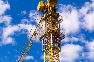 Fototapeta na wymiar Construction of buildings using a tower crane. Construction equipment. Tower crane and blue sky clouds. Lifting of building structures and materials to a height using a tower crane.