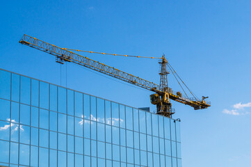 Construction of buildings using a tower crane.  A tower crane and a building with mirror panels....