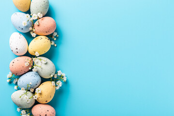 Easter quail eggs and springtime flowers over blue background. Spring holidays concept with copy space. Top view
