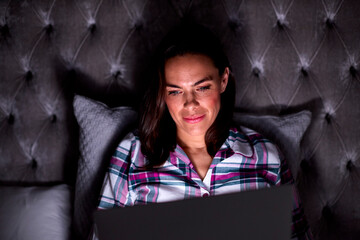Smiling Woman At Home Sitting In Bed Using Laptop At Night