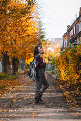 Fototapeta na wymiar Autumn portrait of an attractive young woman on a city street with yellow tree leaves, outdoors